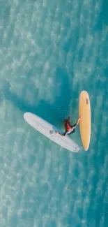 Aerial view of a surfer navigating vibrant aquamarine waters with two surfboards.