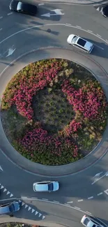 Aerial view of a lively city roundabout with pink flowers and traffic.