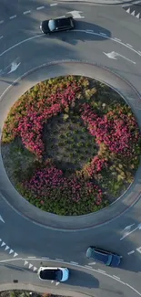 Aerial view of a roundabout with pink flowers and cars.