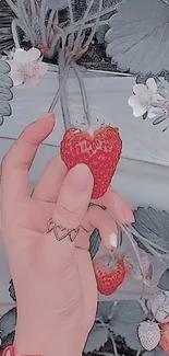 Hand holds a strawberry with muted leaves in the background.