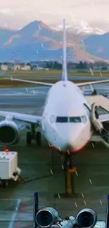 Airplane parked on rainy runway with mountain backdrop.