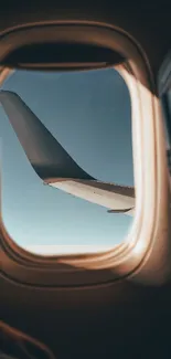 Airplane wing view through window with clear blue sky.