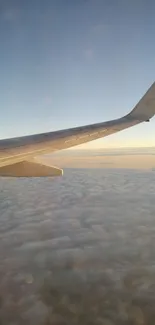 Airplane wing view over clouds during sunrise, captured from a window seat.