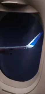 View of airplane wing at night from a window, with a dark blue sky backdrop.