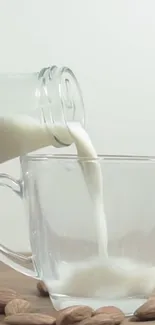 Pouring almond milk into a clear glass cup with almonds around.