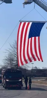 American flag hoisted by two ladder trucks in an outdoor urban area.