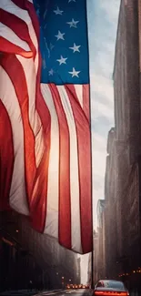 American flag drapes over city street at dusk with car lights.