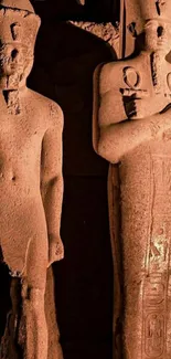 Ancient Egyptian statues in dim lighting on wallpaper.