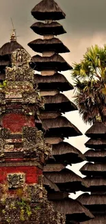 Balinese temple with pagoda roofs and a palm tree against cloudy sky.