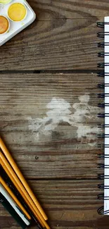 Open notebook with brushes on a wooden desk beside watercolors.