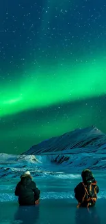 Aurora borealis lights up the night sky over a snowy landscape with two people.