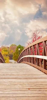 Wooden bridge surrounded by autumn foliage under a cloudy sky.