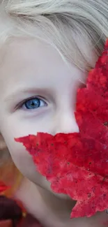 Child peeks from behind a vibrant red autumn leaf.