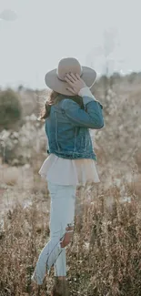 Person in denim jacket in autumn field with beige tones.