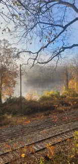 Autumn forest with mist over calm lake and railway in foreground.