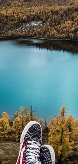 Feet dangle over blue lake surrounded by autumn trees.