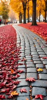 Vibrant autumn path lined with fallen red and yellow leaves on cobblestone.