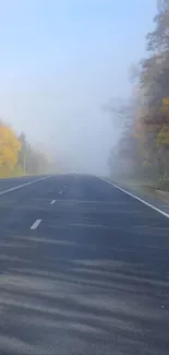 Serene autumn road with morning fog and colorful trees in the background.