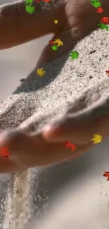 Hand releasing sand with colorful autumn leaves.