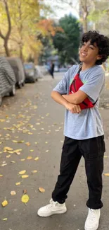 Young person smiling in an autumn street filled with leaves.