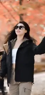 Woman walking in a park with autumn leaves and stylish outfit.