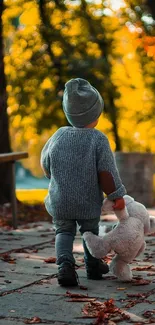 Child walking in autumn holding a teddy bear.