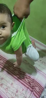 Adorable baby in a green onesie being gently lifted.