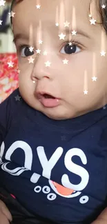 Cute baby in a dark blue shirt amid star effects in wallpaper.