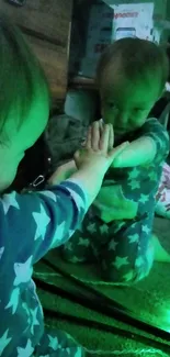 Baby in star pajamas reflecting in mirror with green lighting.