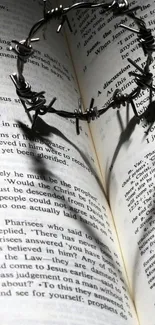 Barbed wire heart shadow on open Bible.