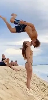 Couple kissing with acrobatic flip on sandy beach.