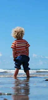 Child enjoys beach with bright blue sky and waves, perfect for serene mobile wallpaper.