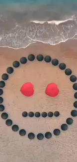 Smiley face made of stones and shells on a sandy beach next to ocean waves.