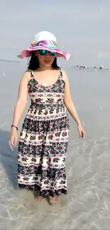 Woman in colorful dress and hat walking along a serene beach.