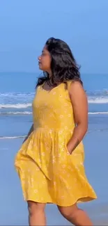 Woman in yellow dress walking along a serene beach with blue sky.