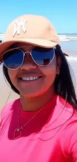 Person in sunglasses and hat smiling at the beach.