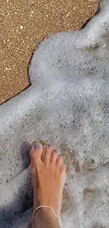 Foot stepping on sandy beach with foamy waves.