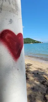 Heart graffiti on a beach with blue sky and distant green hills.