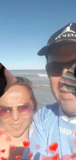 Beach couple selfie with heart overlay.