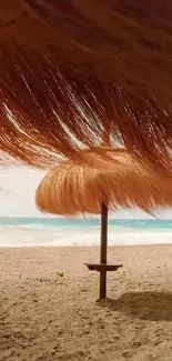 Beach with straw umbrella and ocean waves, sandy brown tones.