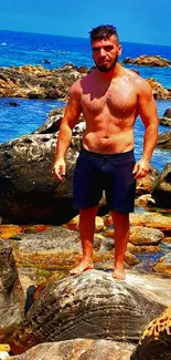 Man standing on rocky beach with blue ocean in background.