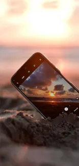 Mobile phone set in sand capturing a breathtaking beach sunset.