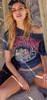 Model in stylish beach attire with a bandana, sitting on sandy beach with poles.