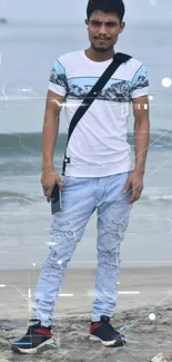 Man on sandy beach with ocean waves in the background, wearing casual summer clothes.