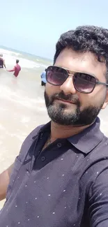 Man taking a selfie on a sunny beach with ocean waves in the background.