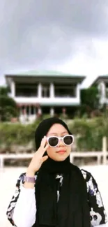 Stylish person in sunglasses on a beach with gray skies.