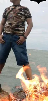 Man in camo with fiery backdrop at beach.