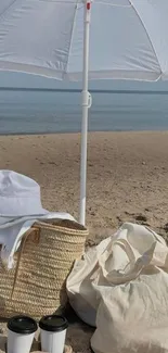 White umbrella and bags on a sandy beach with ocean in the background.