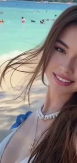 A smiling woman on a beach with turquoise sea.