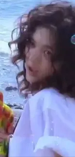 Woman with curly hair at the beach holding a colorful toy.